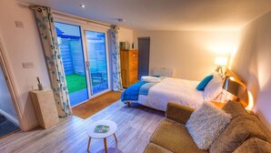 A bedroom with a bed, a sofa, a small table, a wooden cabinet, and a sliding glass door leading to a balcony. - 1 Bed Cabin. Parking. Private & secure Garden. Pets welcome. Nr to beaches/walks (Goldsithney)