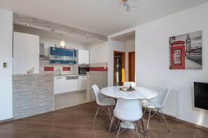 Una cocina moderna con armarios blancos, una isla azul y una zona de comedor con mesa y sillas blancas.
