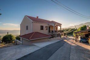 Une maison à deux étages, avec un toit recouvert de tuiles rouges, un balcon et une vue sur le paysage environnant.
