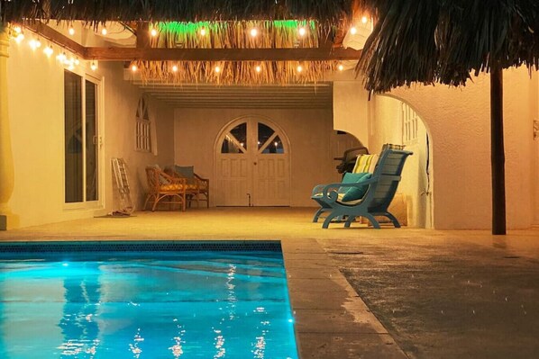 A pool area with a clear blue pool, two lounge chairs, and a door with a decorative archway.