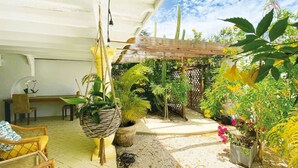 Eine überdachte Terrasse mit Holztisch und -stühlen, umgeben von verschiedenen Blumentöpfen und Blumen.