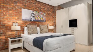 Ein modernes Schlafzimmer mit Backsteinwand, einem großen Bett, einem weißen Kleiderschrank und einem Flachbildfernseher.