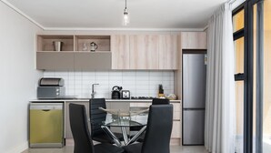A modern kitchen with a glass dining table, black chairs, and a built-in dishwasher. - Modern and Light Apartment in Century City (Cape Town)
