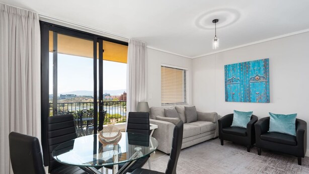 A modern living room with a glass table, black chairs, a grey sofa, and a balcony with a city view. - Modern and Light Apartment in Century City (Cape Town)