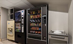 A vending machine with snacks and drinks, a water dispenser, and a trash bin. - Surestay Plus Hotel by Best Western Tulsa East (Tulsa)