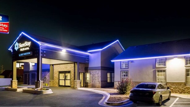A hotel with a sign reading 'SureStay PLUS Hotel by Best Western,' featuring a modern design with stone and brick facade, and a parking lot with a car. - Surestay Plus Hotel by Best Western Tulsa East (Tulsa)