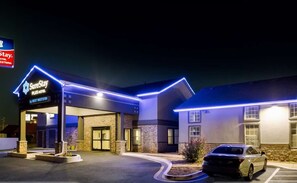 A hotel with a sign reading 'SureStay PLUS Hotel by Best Western,' featuring a modern design with stone and brick facade, and a parking lot with a car. - Surestay Plus Hotel by Best Western Tulsa East (Tulsa)