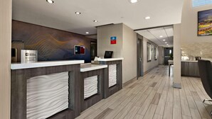 Zona d'entrada d'hotel amb disseny modern, que inclou una taula de recepció, una pantalla digital i una paret amb un dibuix decoratiu.