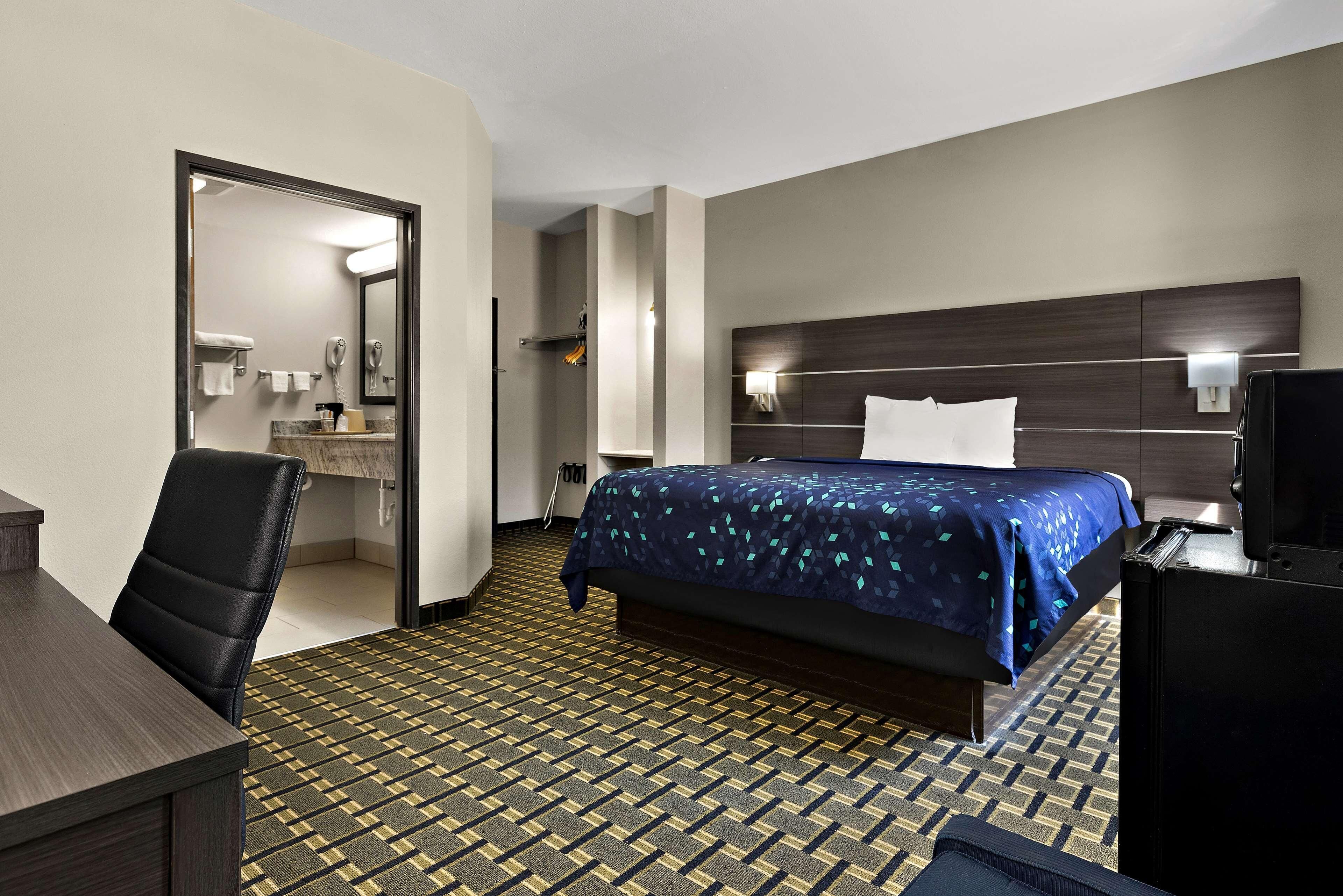 A hotel room with a bed, a desk, a chair, a TV, and a bathroom visible through an open door.