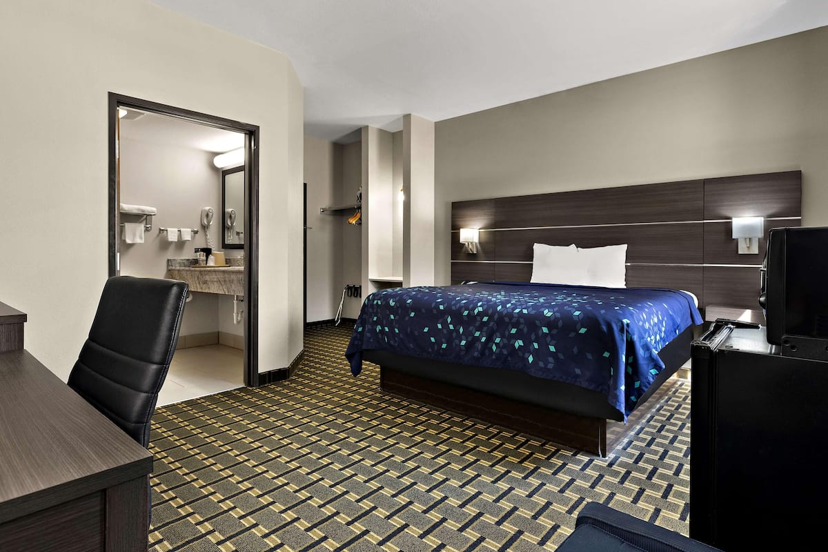 Ein Hotelzimmer mit Bett, Schreibtisch, Stuhl, Fernseher und einem durchgegangenen Tür sichtbaren Badezimmer.