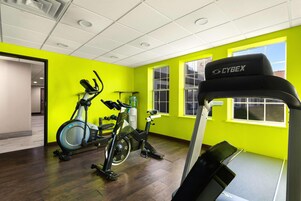 Un gimnasio con equipo de ejercicio, paredes amarillo brillante y ventanas amplias.