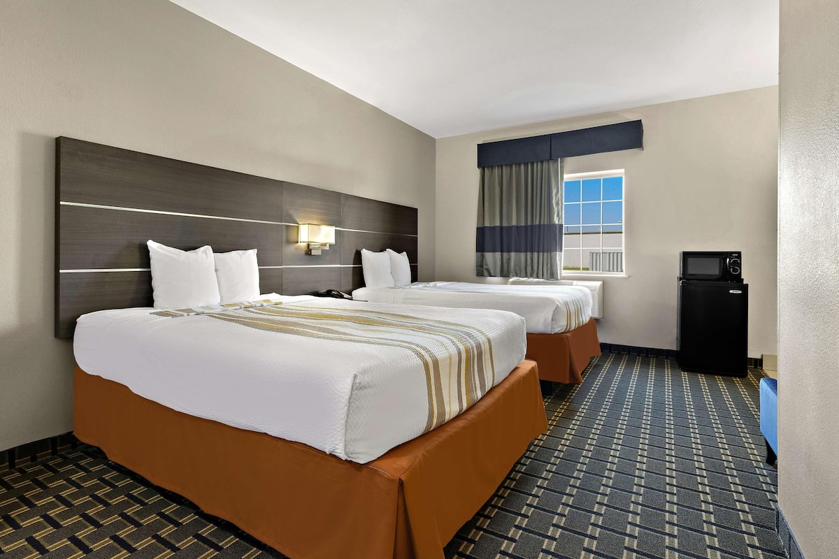 A hotel room with two beds, a television, and a window with curtains.