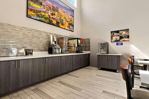 A modern kitchen with a coffee machine, a microwave, and a coffee press. There is a tiled backsplash and a painting of a cityscape on the wall. - Surestay Plus Hotel by Best Western Tulsa East (Tulsa)