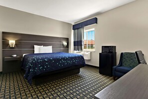 Quarto de hotel com cama, escrivaninha, cadeira, televisão e janela com cortinas.
