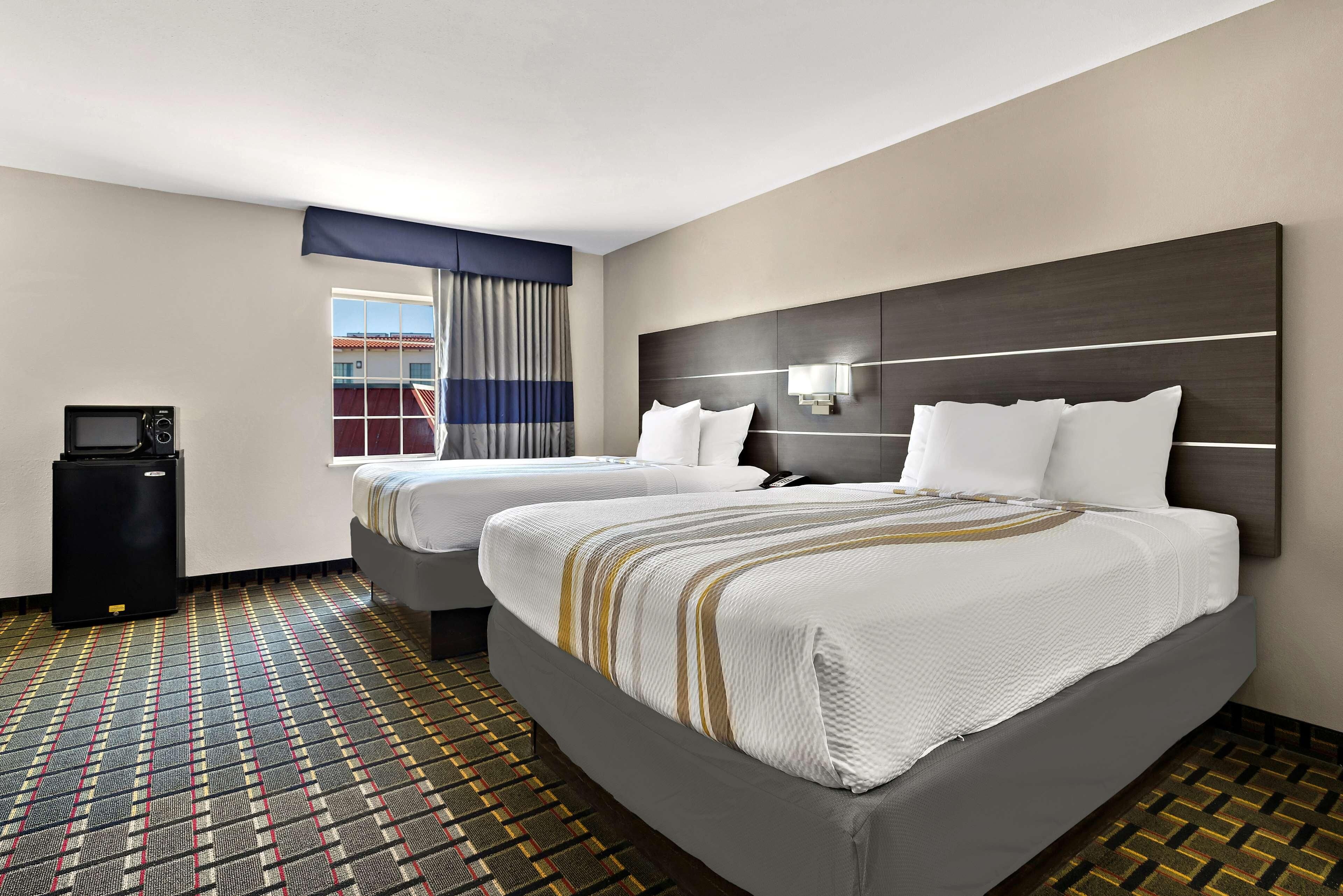 A hotel room with two beds, a microwave, a small table, and a window with curtains.
