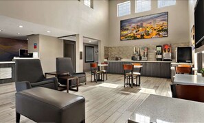 Een hotel lobby met zitplaatsen, een keukenhoek en een groot schilderij aan de muur.