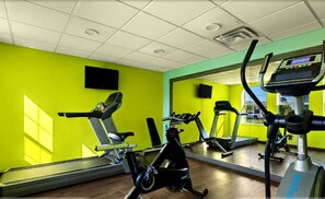 Een sportschool met trainingsapparatuur, een grote spiegel en felgroene wanden.
