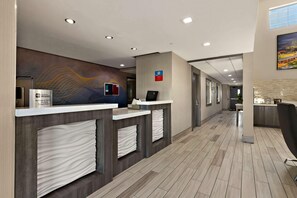 Een hotel receptie met een modern design, bestaande uit een receptiebalie, een digitaal scherm en een wand met een decoratief patroon.