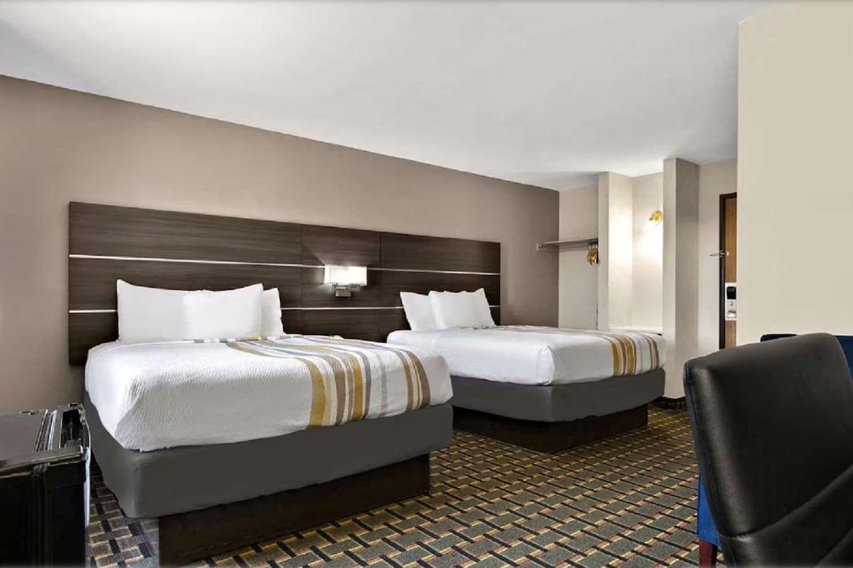 Ein Hotelzimmer mit zwei Betten, einem Schreibtisch, einem Stuhl und einem gemusterten Boden.