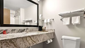 A modern bathroom with a granite countertop, a large mirror, a towel rack, and a toilet. - Surestay Plus Hotel by Best Western Tulsa East (Tulsa)