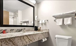 A modern bathroom with a granite countertop, a large mirror, a towel rack, and a toilet. - Surestay Plus Hotel by Best Western Tulsa East (Tulsa)