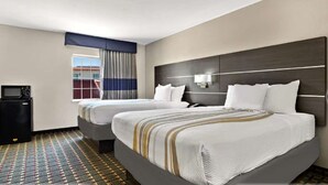 A hotel room with two beds, a small desk with a microwave, a window with curtains, and a patterned floor. - Surestay Plus Hotel by Best Western Tulsa East (Tulsa)