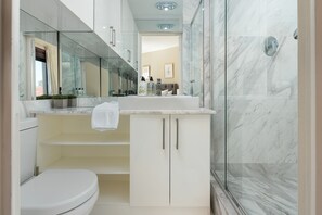 A modern bathroom with a glass shower enclosure, a white toilet, and a vanity with a mirror and countertop.