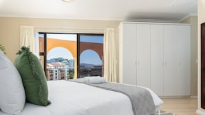 A hotel room with a large bed, a wardrobe, and a view of buildings through a glass door.