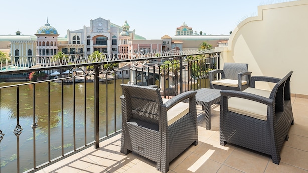 A balcony with wicker furniture overlooking a body of water and buildings with domed roofs.