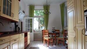 A kitchen with wooden cabinets, a dining table with chairs, a chandelier, and a window with curtains. - Gohlis city apartment (Leipzig)