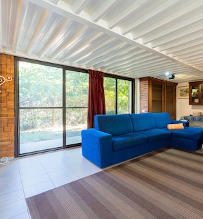 A modern living room with a blue sofa, a large sliding glass door, and a patterned rug. - Domus Sol Aria 2 (Castiadas)