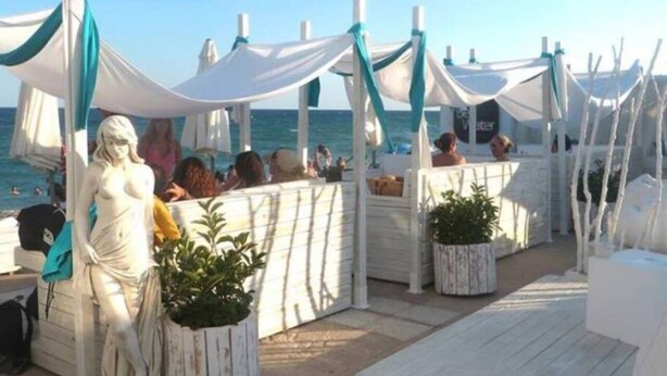 Eine Terrassenanlage am Strand mit weißen Markisen, einer Statue und Kübelpflanzen.