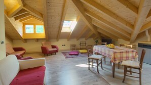 Una habitación cálida en el ático, con vigas de madera, una mesa de comedor con sillas y un sofá.