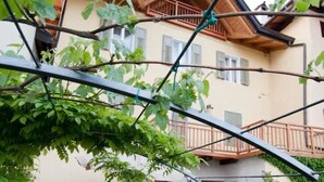 Un patio con suelo de piedra, sillas blancas y un pequeño jardín.