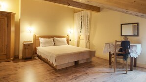 Un dormitorio con una cama de madera, una mesita de noche, una silla, una mesa con mantel de encaje y un espejo en la pared.