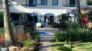 A modern house with a swimming pool, surrounded by tropical plants and palm trees. - Brisa do Mar Barê Praia Hotel (São Sebastião)
