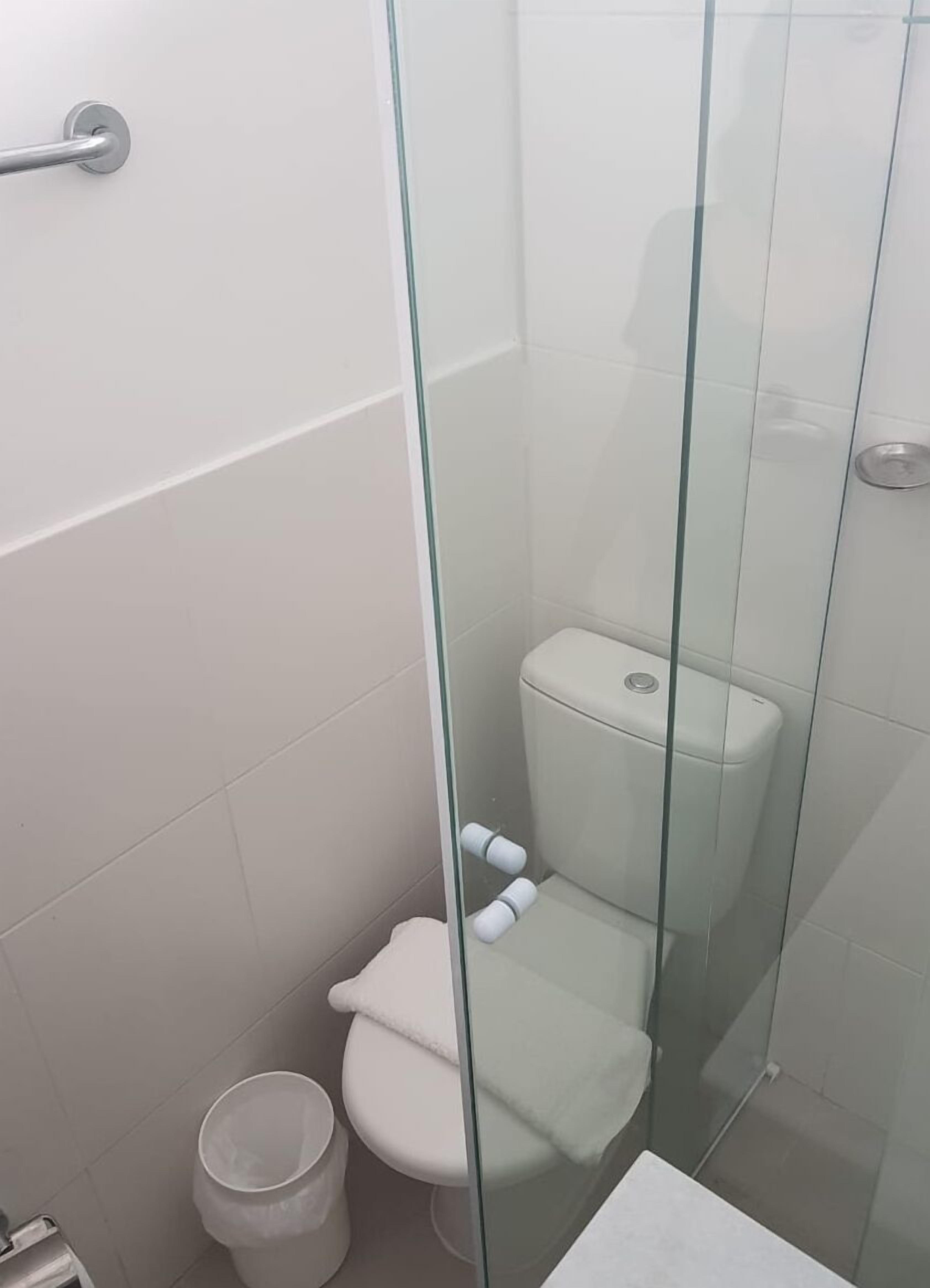 Ein kleines, separates Badezimmer mit Toilette, einer Glasabtrennung und einer weißen Mülltonne.