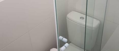 Une petite salle de bain fermée, comprenant des toilettes, une cloison en verre et une poubelle blanche.