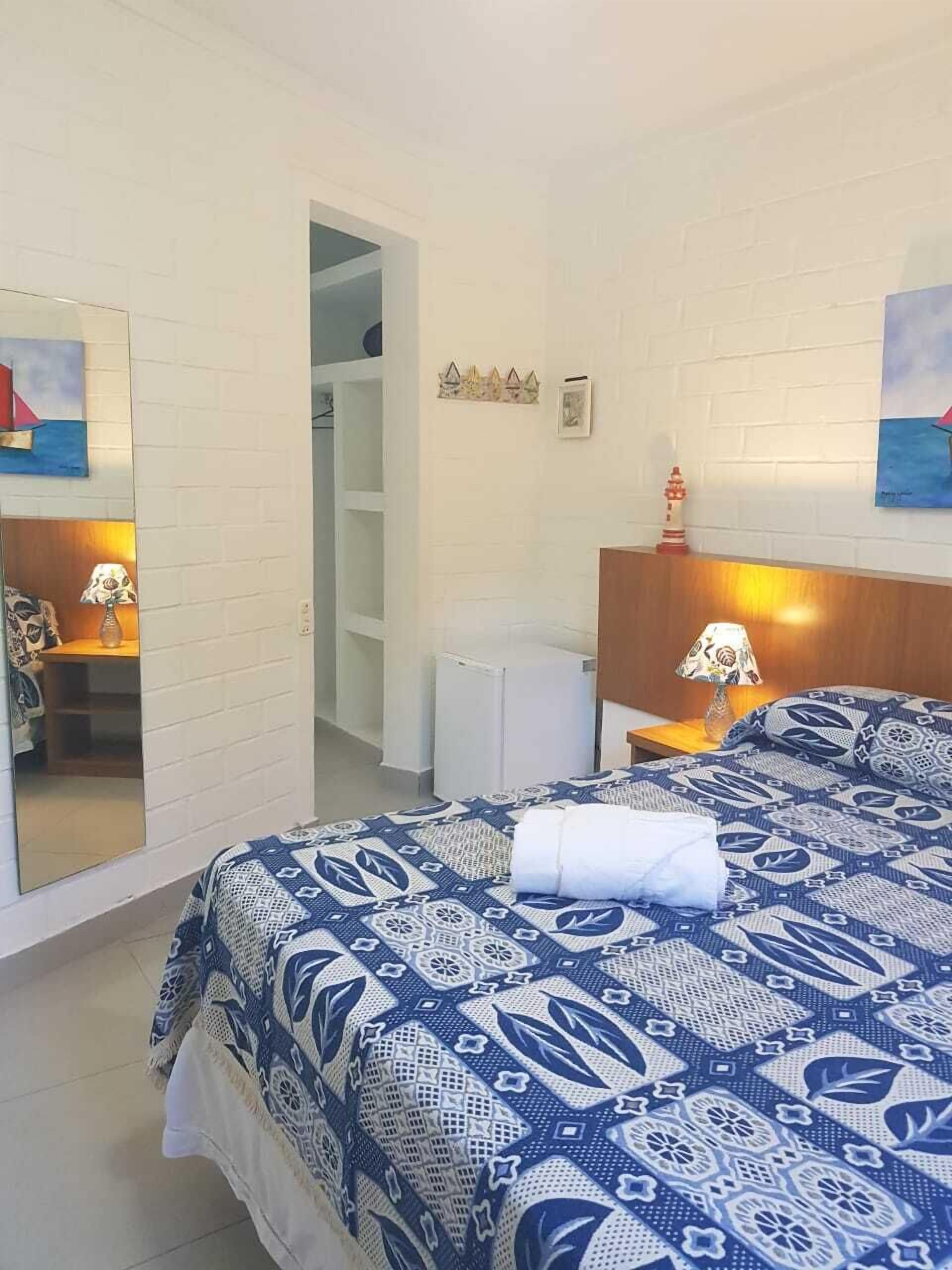 Una habitación de hotel con una cama, una mesita de noche, una lámpara, un espejo y un armario.