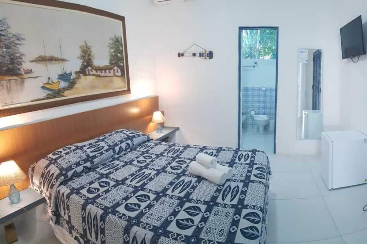 Ein Schlafzimmer mit einem Bett, einer Nachttischlampe, einem Gemälde, einem Fernseher und einer Tür zu einem Badezimmer.