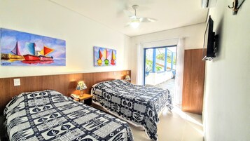 Habitación de hotel con dos camas, un ventilador de techo, un cuadro de veleros, una ventana con vistas y un televisor montado en la pared.