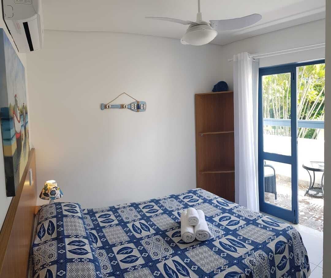 A bedroom with a bed, a ceiling fan, a wall-mounted shelf, and a door leading to an outdoor area.