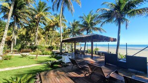 A beachside patio with outdoor seating, palm trees, and a view of the ocean. - Brisa do Mar Barê Praia Hotel (São Sebastião)