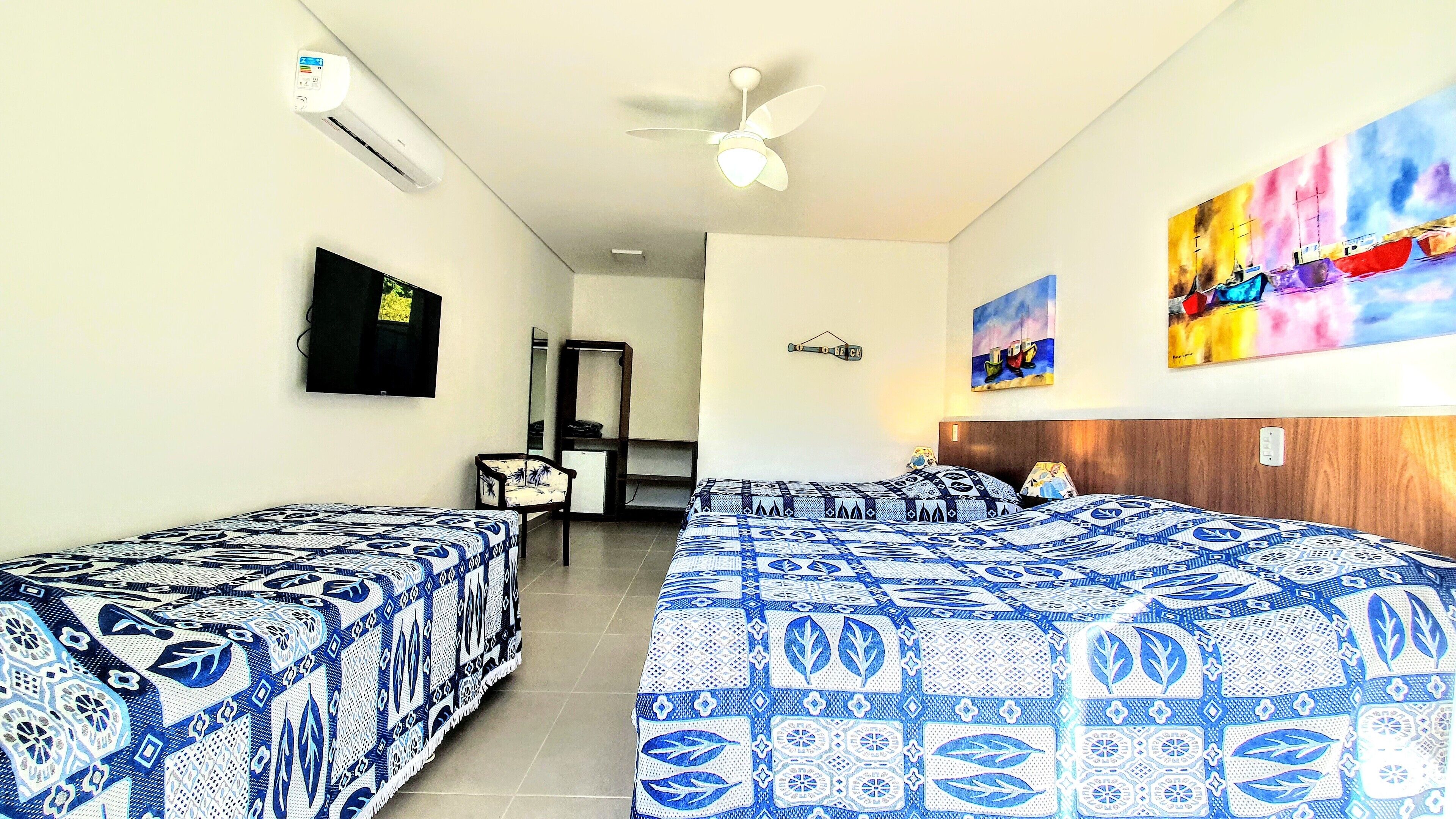 A hotel room with two beds, a TV, a ceiling fan, and artwork on the walls.