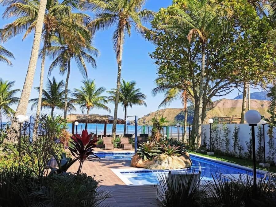 Un área de piscina con palmeras, una formación rocosa y vista al océano.