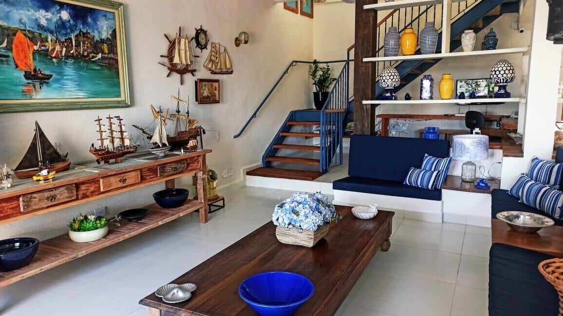 Una sala de estar con una mesa de centro de madera, cuencos azules, un sofá con cojines a rayas, una escalera con barandas azules y un estante con adornos.