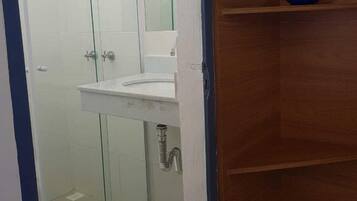 A bathroom with a glass shower enclosure, a white sink, and a wooden shelf.