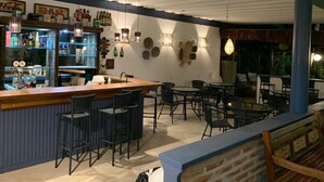A bar area with a counter, bar stools, and various bottles. There are tables and chairs arranged around the bar. - Brisa do Mar Barê Praia Hotel (São Sebastião)