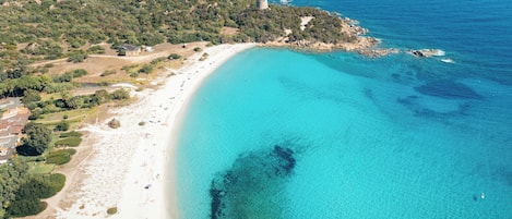 An aerial view of a coastal area with a beach, a tower, and surrounding greenery.