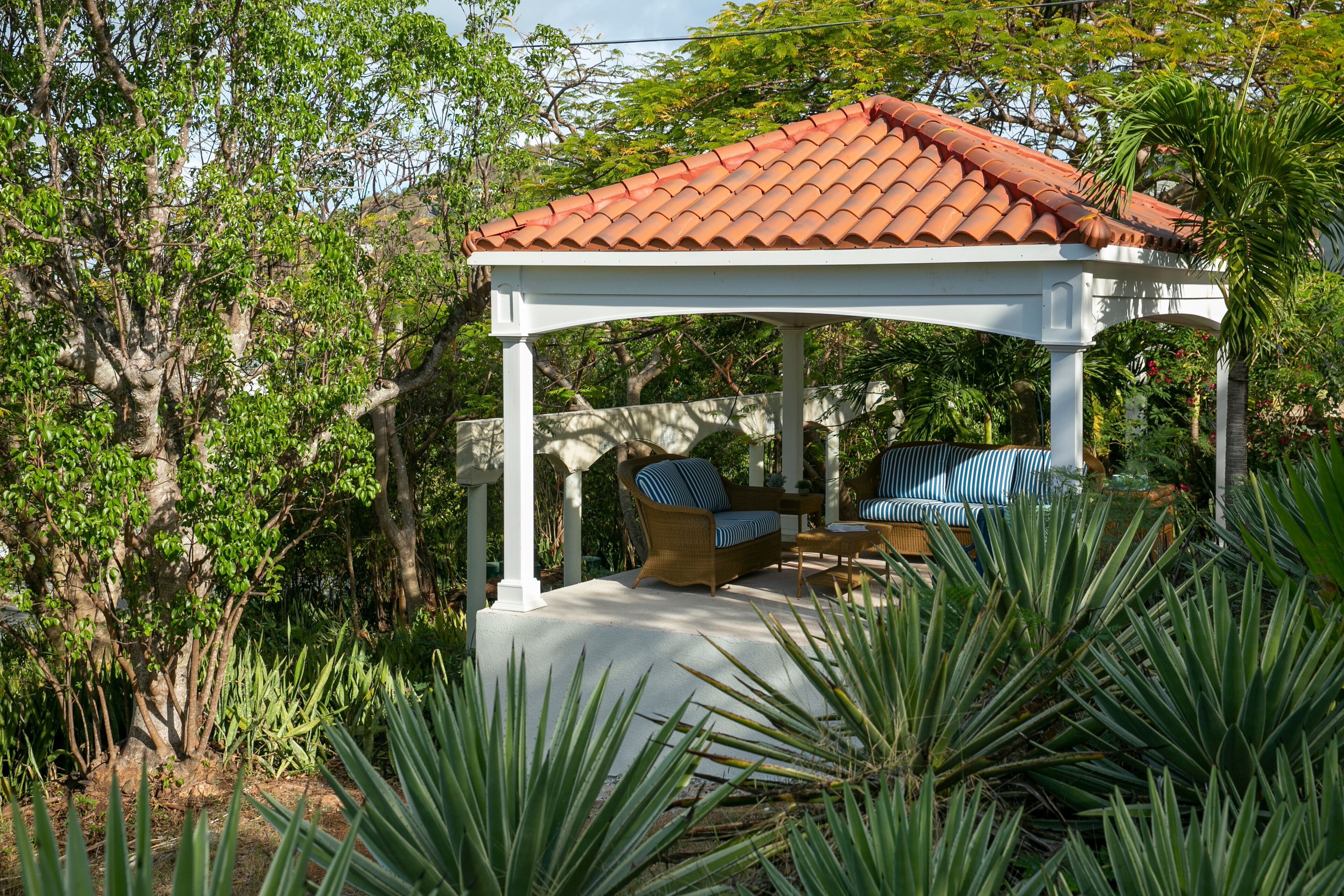 A gazebo with a tiled roof, surrounded by lush greenery and trees.